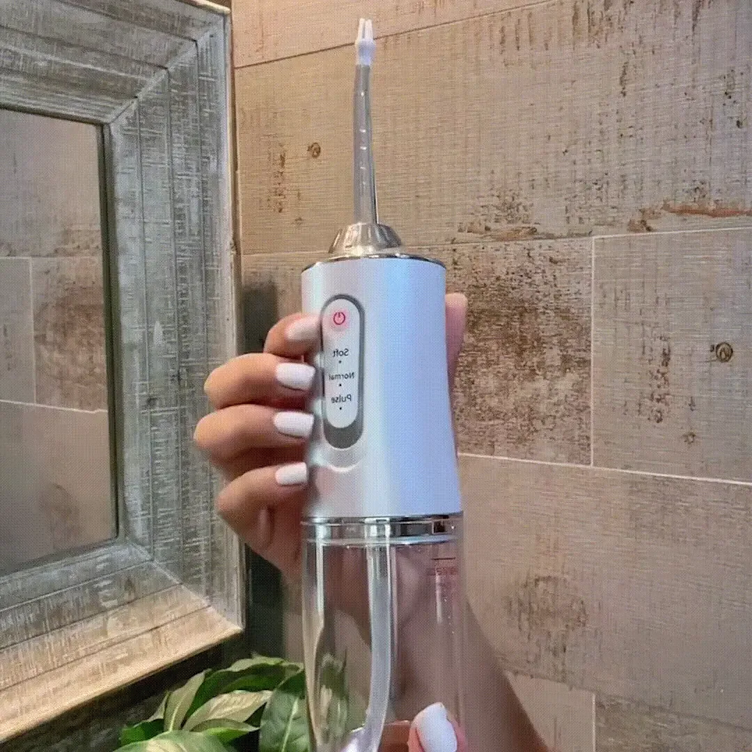 Mano sosteniendo el irrigador bucal blanco frente a un espejo